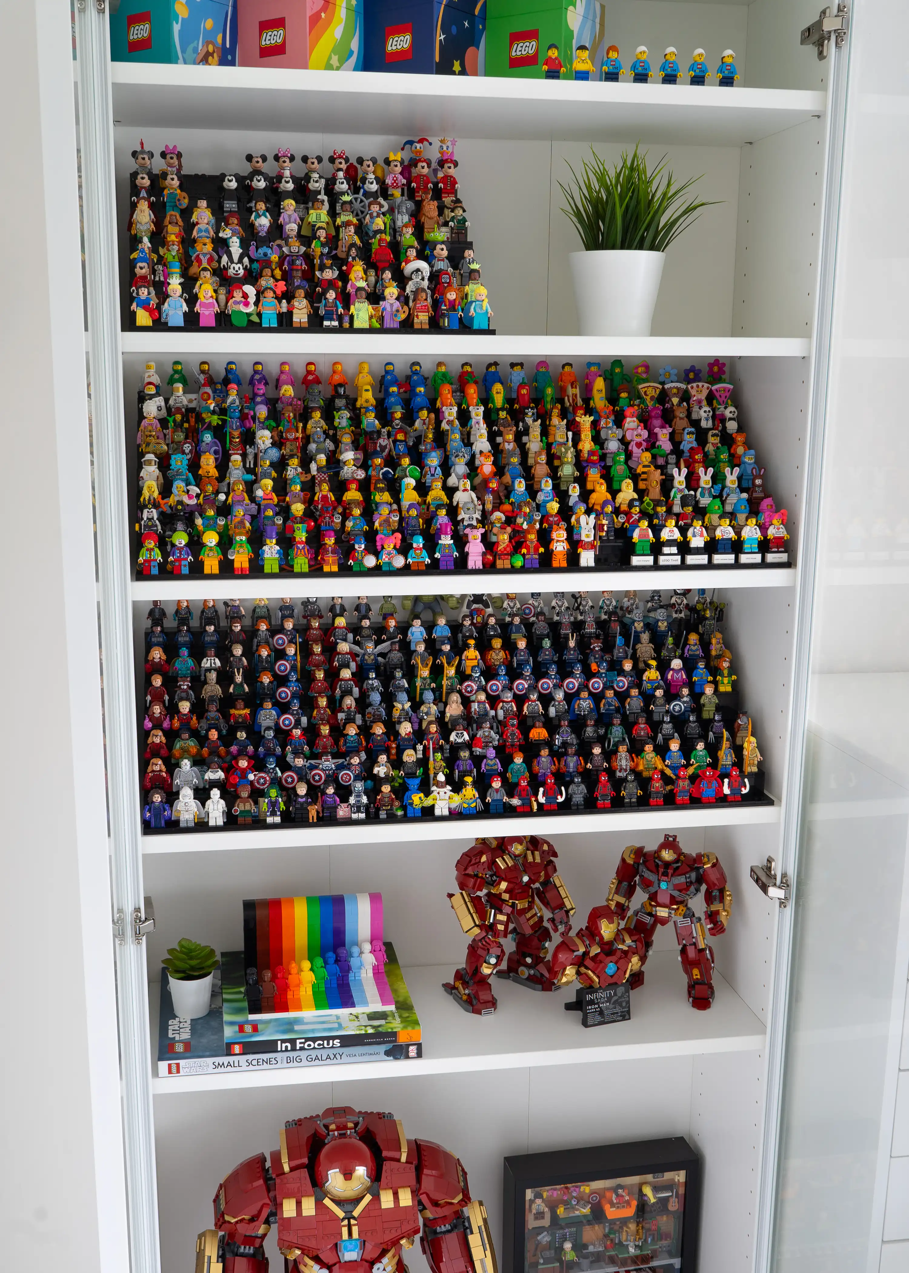 A neatly organized display shelf featuring hundreds of LEGO minifigures, from Disney characters to Marvel superheroes, alongside larger builds like Hulkbusters and the Everyone Is Awesome set