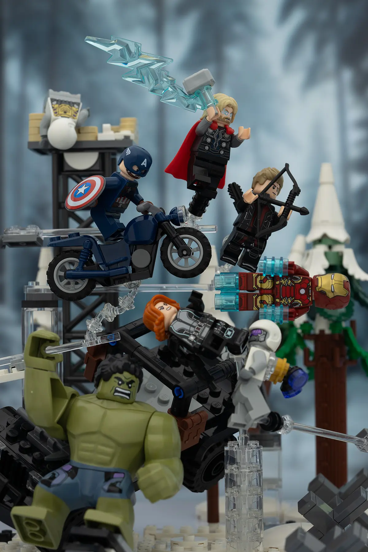 LEGO Avengers minifigures in an action-packed snowy forest diorama. Hulk, Thor, Captain America, Iron Man, Hawkeye, Black Widow, and others are dynamically posed mid-battle using clear plastic stands and support elements, which are still visible.