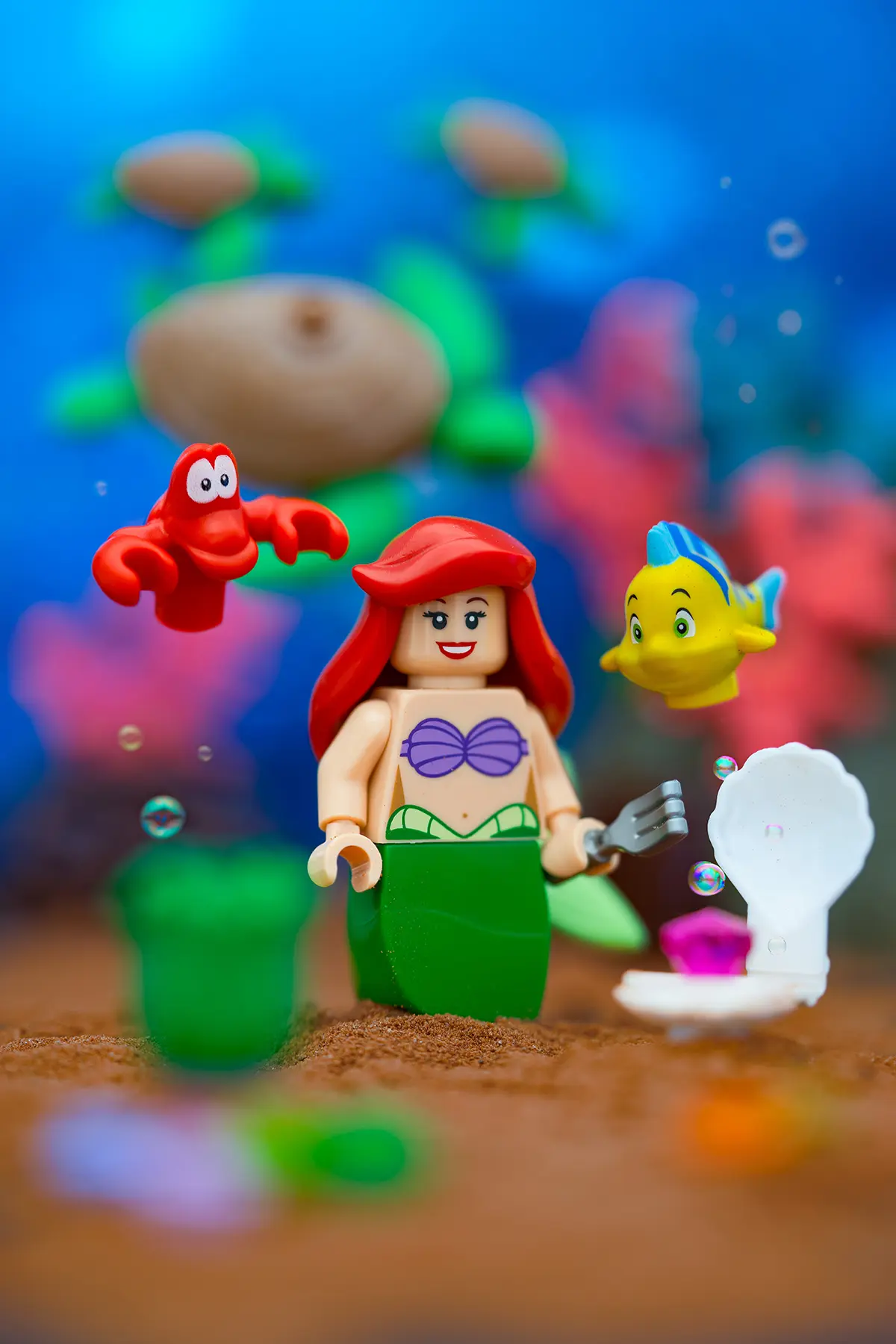 Ariel, Sebastian, and Flounder appear to float freely in a vibrant underwater LEGO scene. Support structures are removed, bubbles are added, and the colors are enhanced to create a lively and magical undersea atmosphere.