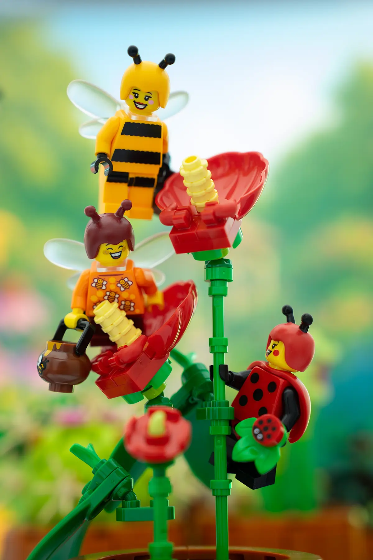 The LEGO bee and ladybug minifigures appear naturally perched or flying around bright red flowers in a vibrant garden. All supports have been removed, enhancing the whimsical and polished look of the scene.
