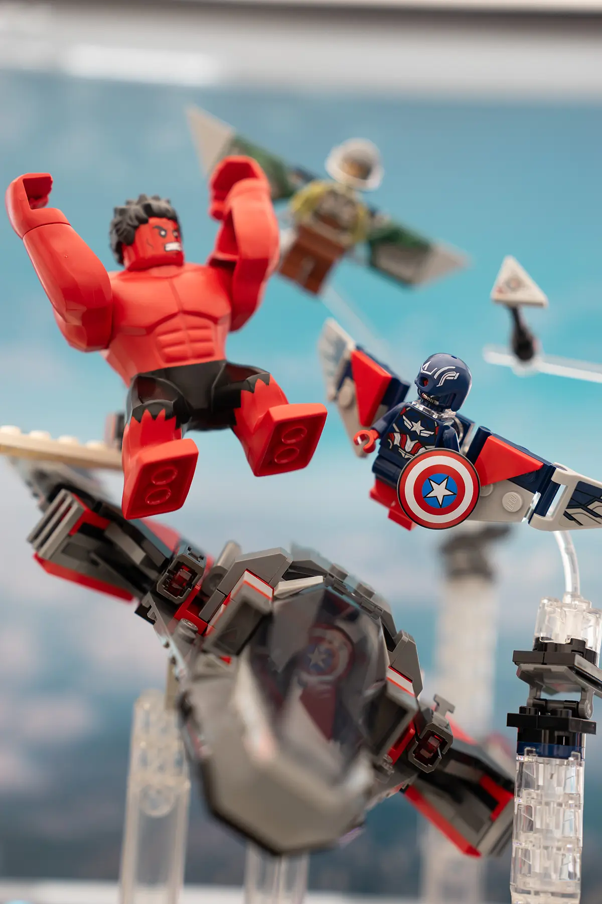 LEGO Red Hulk, Sam Wilson Captain America, Falcon, and a jet are positioned in mid-air, supported by clear rods and stands. The background features a bright blue sky, evoking a high-altitude showdown.