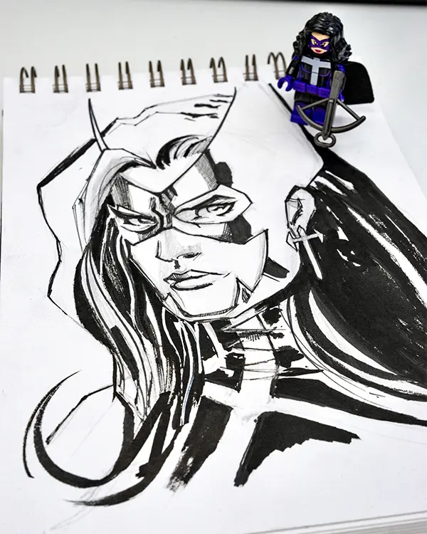 LEGO Huntress minifigure displayed beside an expressive ink drawing of the DC vigilante.